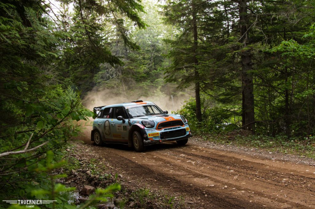 Mini Cooper sur une piste de terre dans la forêt qui prend un virage